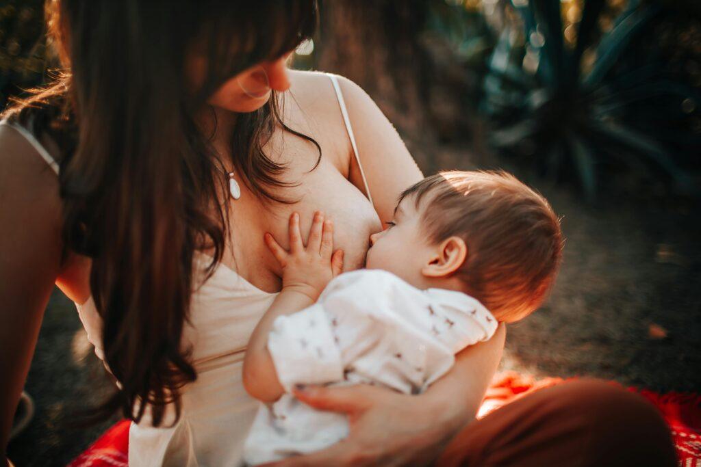 Breast Lumps After Weaning: A tender moment of a mother breastfeeding her baby outdoors in natural light.